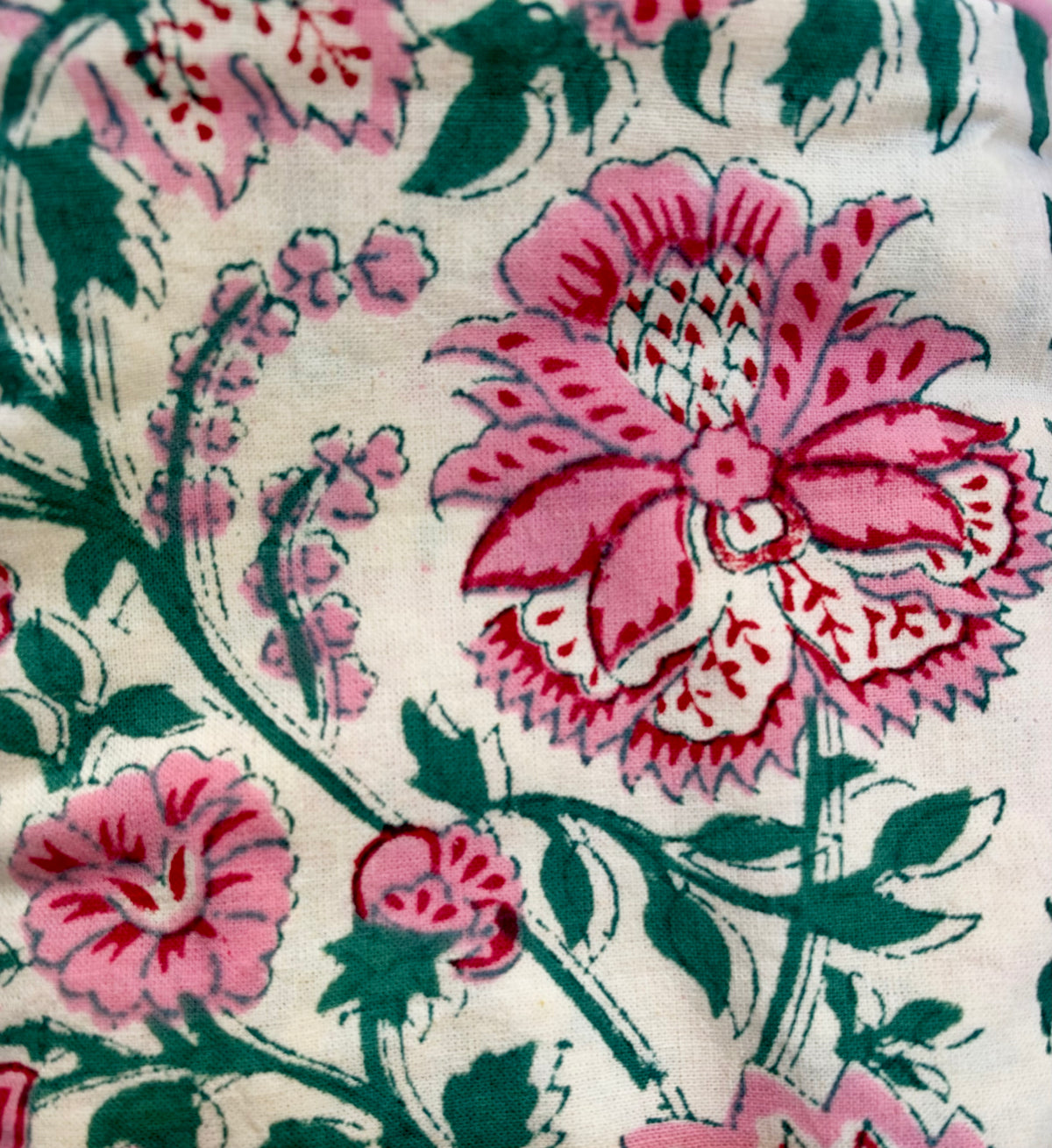 A close-up of a floral fabric print featuring pink flowers and green leaves on a cream background.