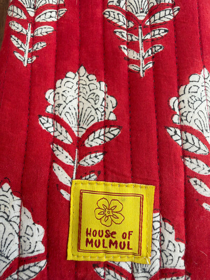 House of Mulmul - Blockprinted Mobile Sling Bag. Close-up of a red quilted textile with a white floral and leaf pattern and a yellow sewn label reading 'HOUSE OF MULMUL'.