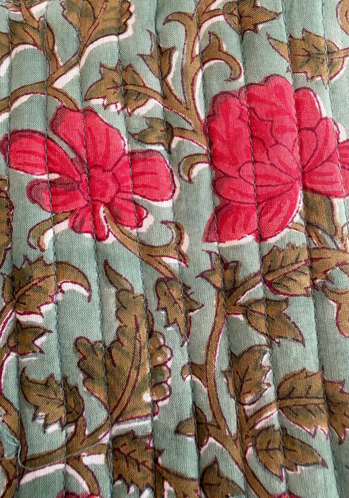 House of Mulmul - Blockprinted Mobile Sling Bag. A close-up of a quilted fabric featuring a floral pattern with bright pink flowers and brown leaves on a muted sage green background.