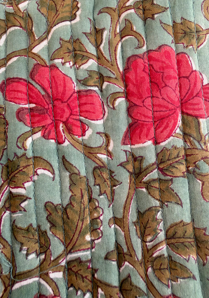 House of Mulmul - Blockprinted Mobile Sling Bag. A close-up of a quilted fabric featuring a floral pattern with bright pink flowers and brown leaves on a muted sage green background.
