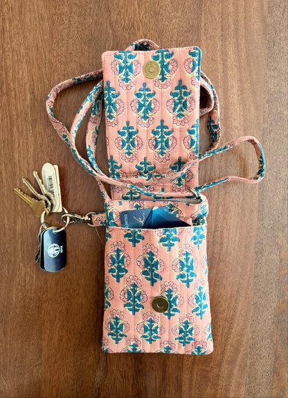 House of Mulmul - Blockprinted Mobile Sling Bag. A pink and teal patterned mobile sling bag holder wallet with a strap, shown open on a wooden surface with keys and cards inside.