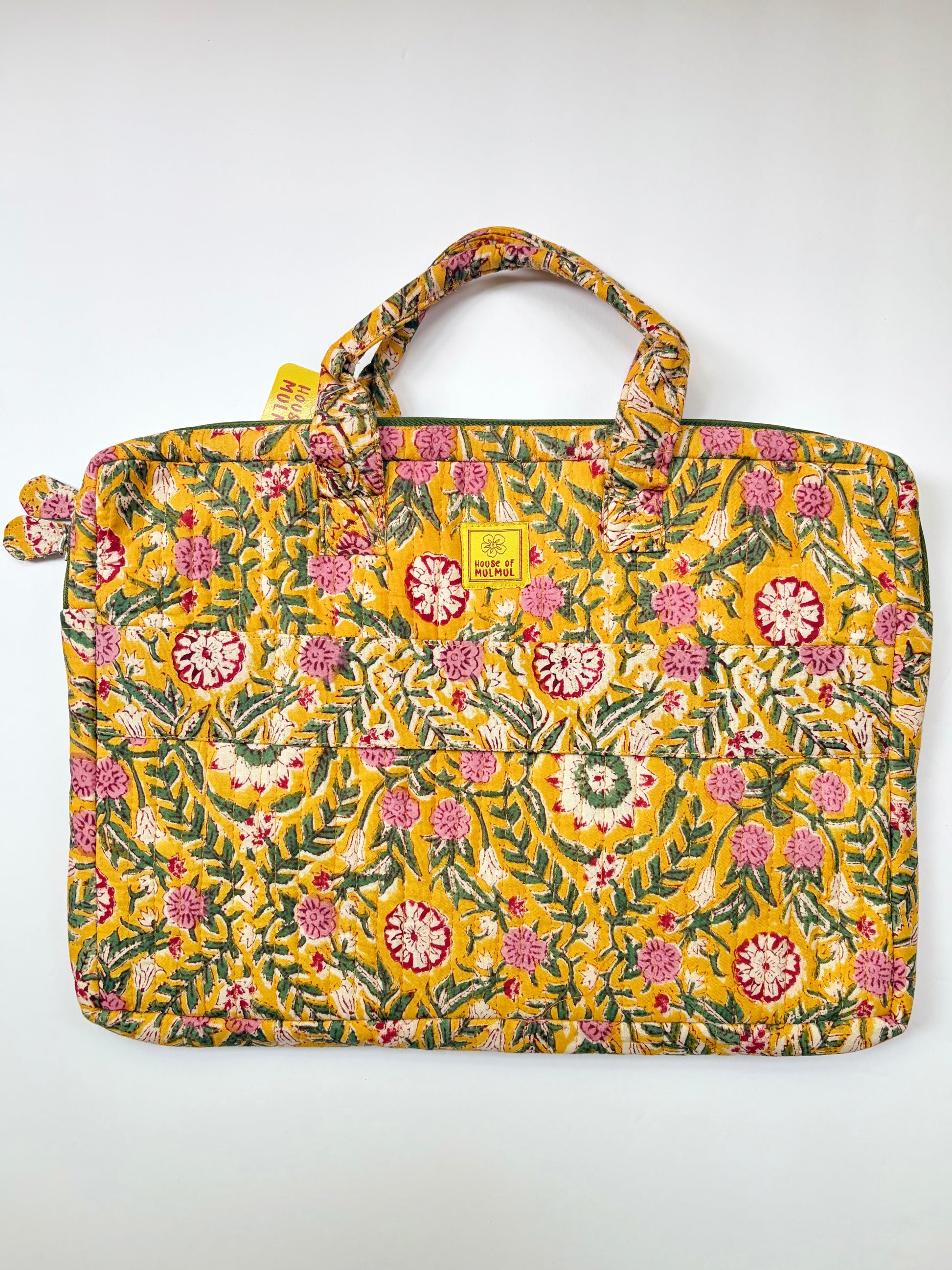 House of Mulmul - Blockprinted Cotton Quilted Laptop Bag. A yellow fabric tote bag with a dense floral and botanical print in pink, green, and white, featuring two top handles and a small yellow brand tag on the front.