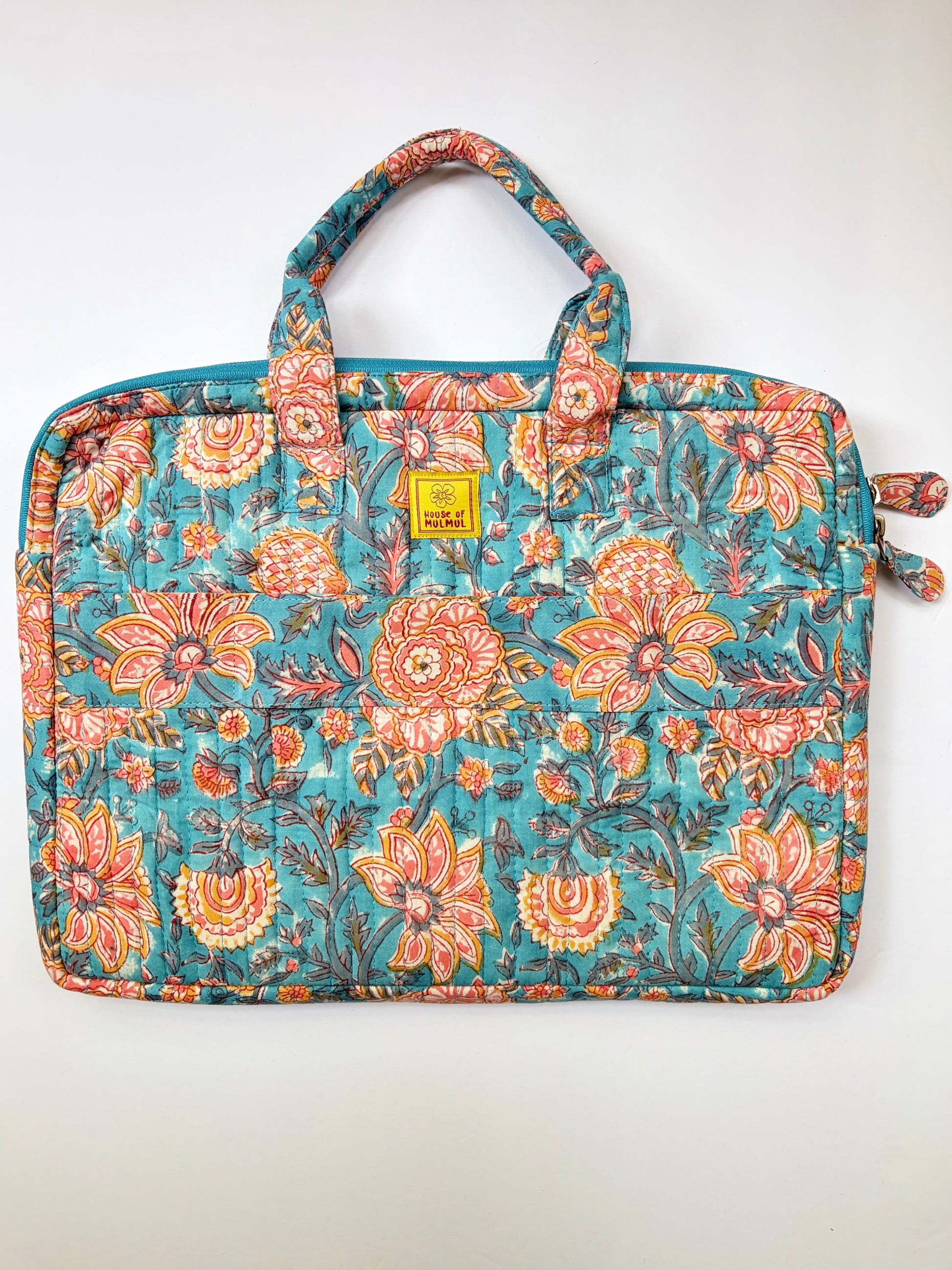 House of Mulmul - Blockprinted Cotton Quilted Laptop Bag. A quilted laptop sleeve featuring a vibrant floral pattern in teal, orange, and pink, with a small yellow brand patch on the front.