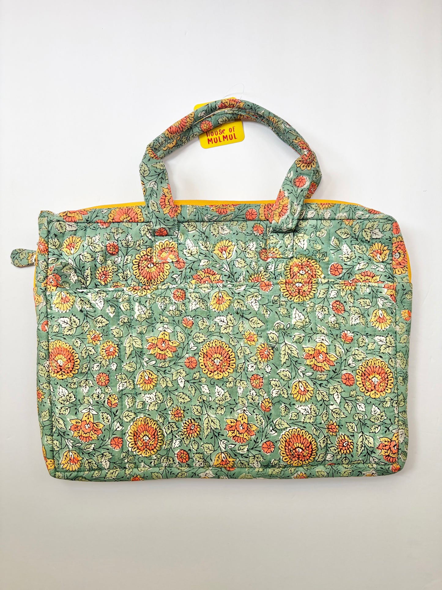 House of Mulmul - Blockprinted Cotton Quilted Laptop Bag. A quilted fabric tote laptop bag featuring a green floral pattern with orange, yellow, and white flowers, complete with two top handles and a small yellow tag.