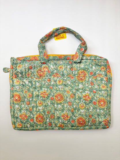 House of Mulmul - Blockprinted Cotton Quilted Laptop Bag. A quilted fabric tote laptop bag featuring a green floral pattern with orange, yellow, and white flowers, complete with two top handles and a small yellow tag.