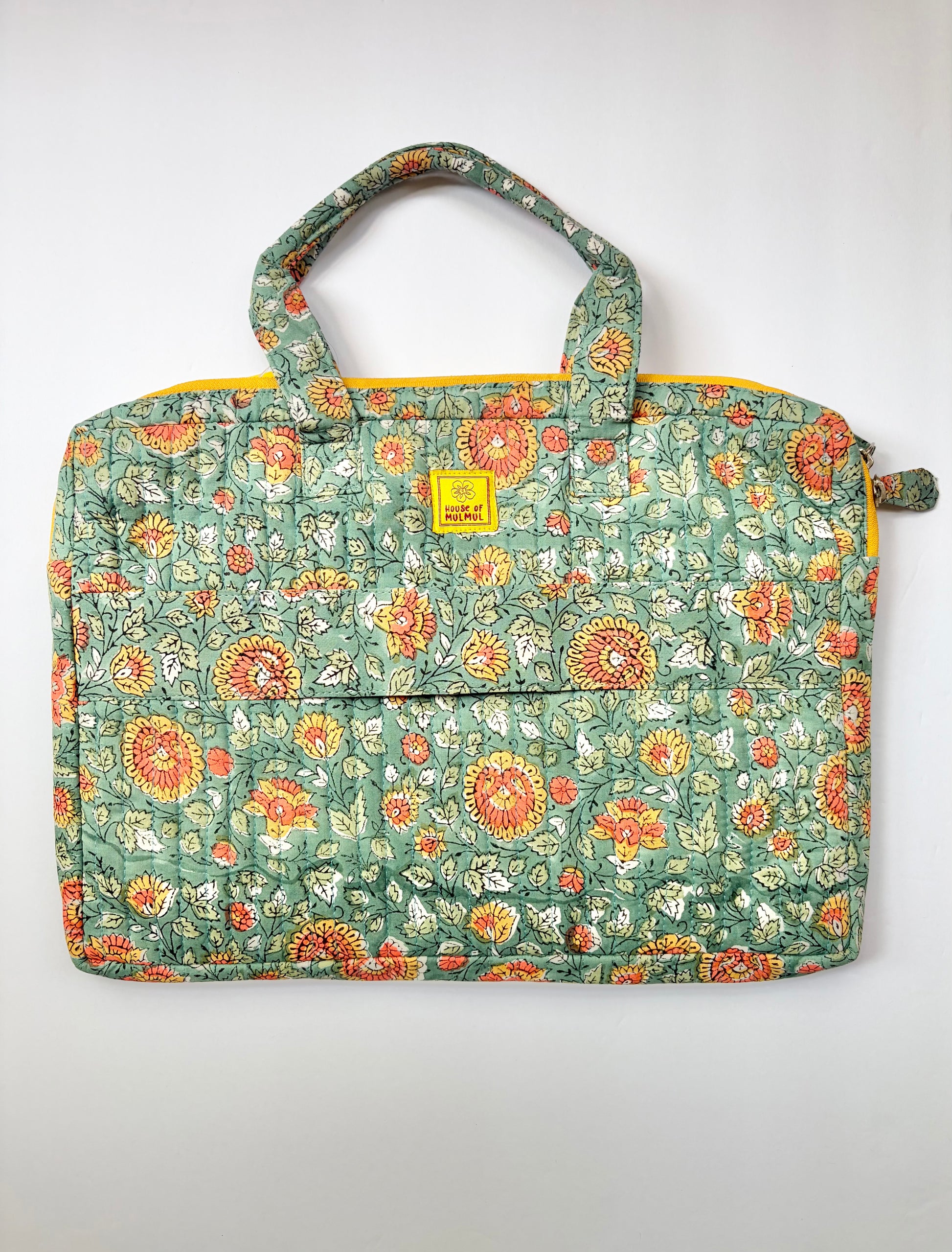 House of Mulmul - Blockprinted Cotton Quilted Laptop Bag. A quilted fabric tote  laptop bag featuring a green base with a dense orange, red, and white floral pattern, complete with two top handles and a small yellow brand label on the front.