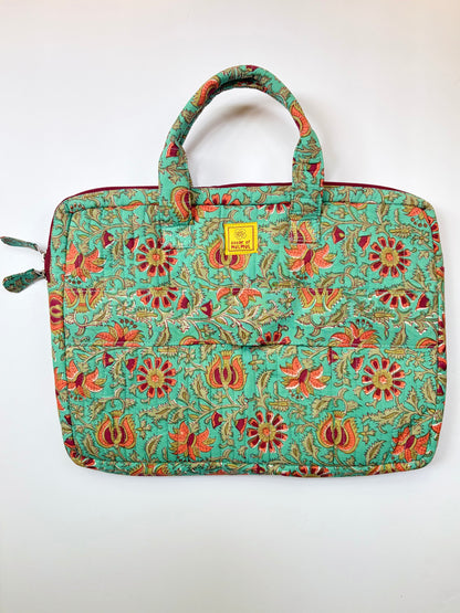 House of Mulmul - Blockprinted Cotton Quilted Laptop Bag. A quilted laptop sleeve featuring a vibrant floral and paisley pattern in turquoise, red, orange, and gold. It has two top handles, a zippered closure, and a small yellow brand label on the front.