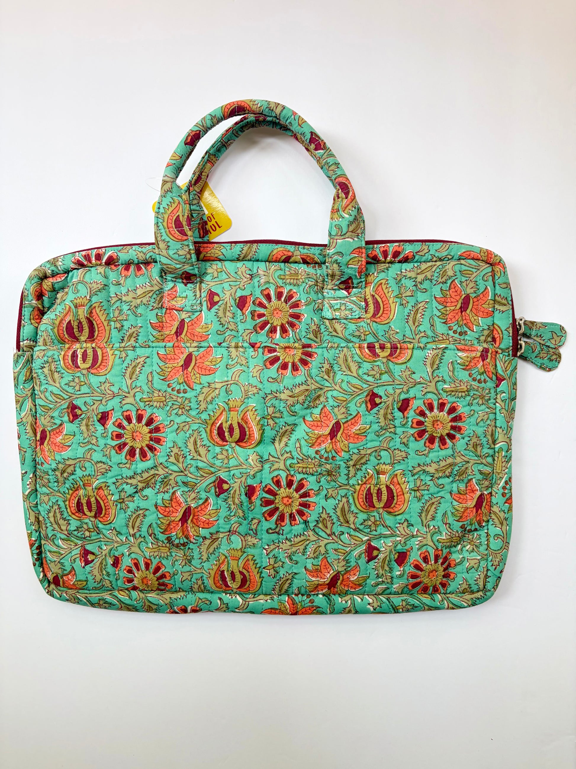 House of Mulmul - Blockprinted Cotton Quilted Laptop Bag. A quilted laptop bag with a vibrant turquoise green background and an all-over floral and paisley block-print pattern in orange, red, and gold, featuring dual top handles and a side strap.
