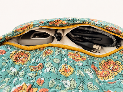House of Mulmul - Blockprinted Cotton Quilted Laptop Bag. Close-up of a floral quilted laptop bag with a yellow zipper, showing its interior compartments containing a gray power bank, a black pen, and a gray cable.