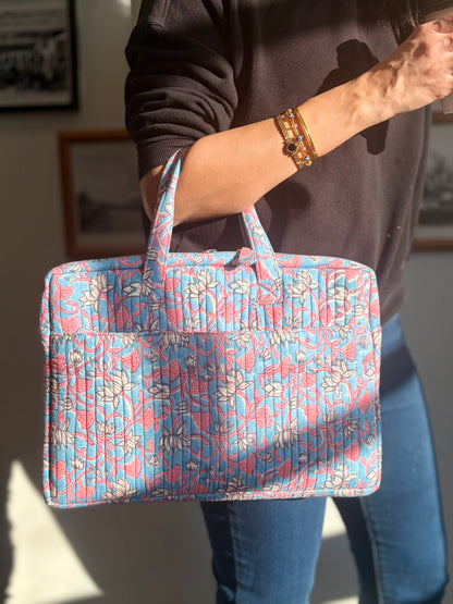 House of Mulmul - Blockprinted Cotton Quilted Laptop Bag. A person holding a quilted laptop bag with a pink and blue floral pattern, shown in a home setting with sunlight casting shadows.