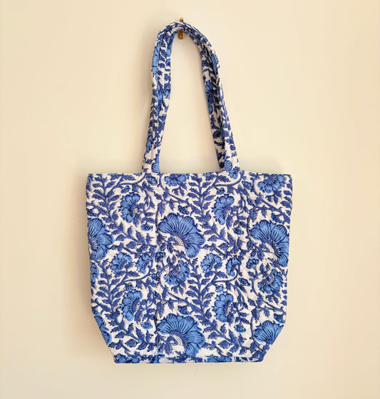 House of Mulmul - Bucket Tapered Tote Bag. A cotton tote bag with a blue and white floral block print pattern, hanging against a solid beige background.