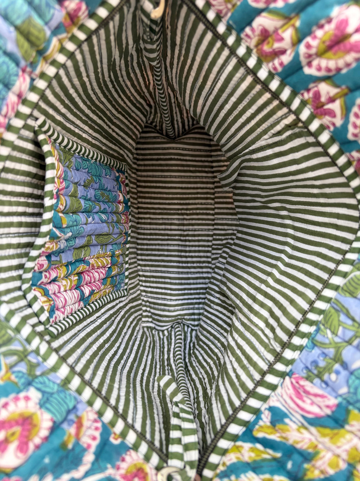House of Mulmul - Bucket Tapered Tote Bag. Close-up of the interior of a quilted fabric bag or basket, showing a striped green and white fabric lining with a colorful floral patterned fabric attached on the left side.