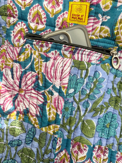 House of Mulmul - Bucket Tapered Tote Bag. Close-up of a quilted fabric bag with a floral print in pink, blue, green, and white, featuring a yellow 'HOUSE OF MULMUL' brand patch and a zipper pocket.
