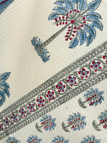 House of Mulmul - Cotton Bath Towel. Close-up of a patterned cotton towel with floral and palm tree designs on a beige background.