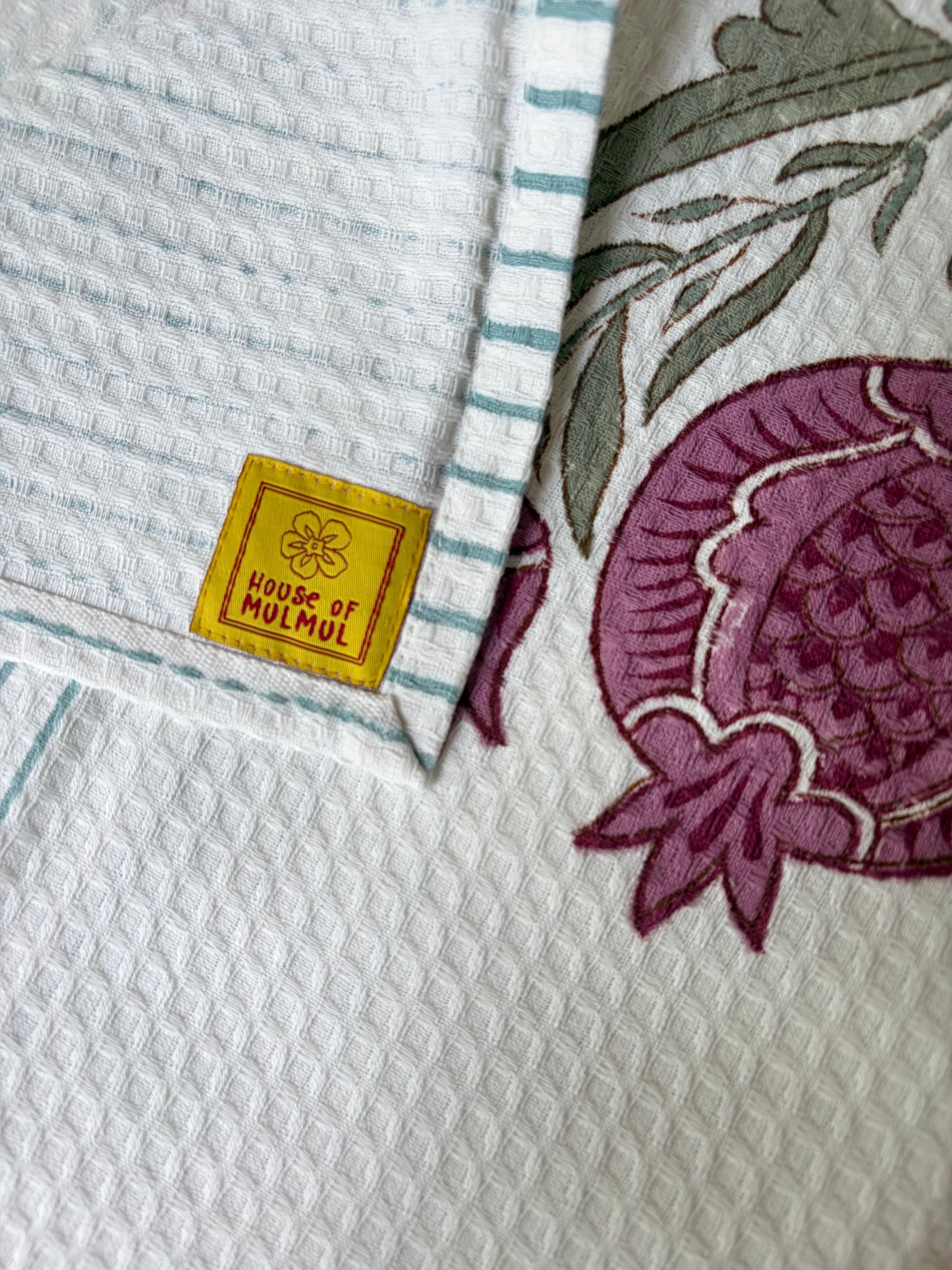 House of Mulmul - Cotton Bath Towel. Hand block printed purple flower and green leaves on a white fabric with 'House of Mulmul' label