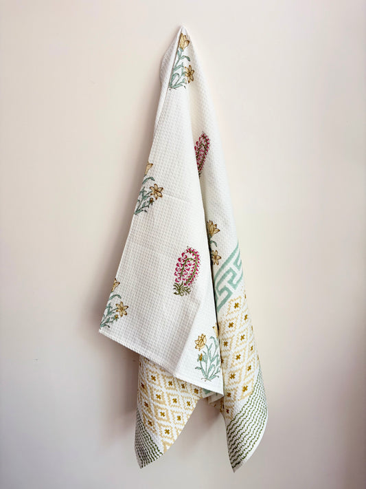 House of Mulmul - Cotton Bath Towel. Floral patterned towel hanging against a plain background with geometric pattern.