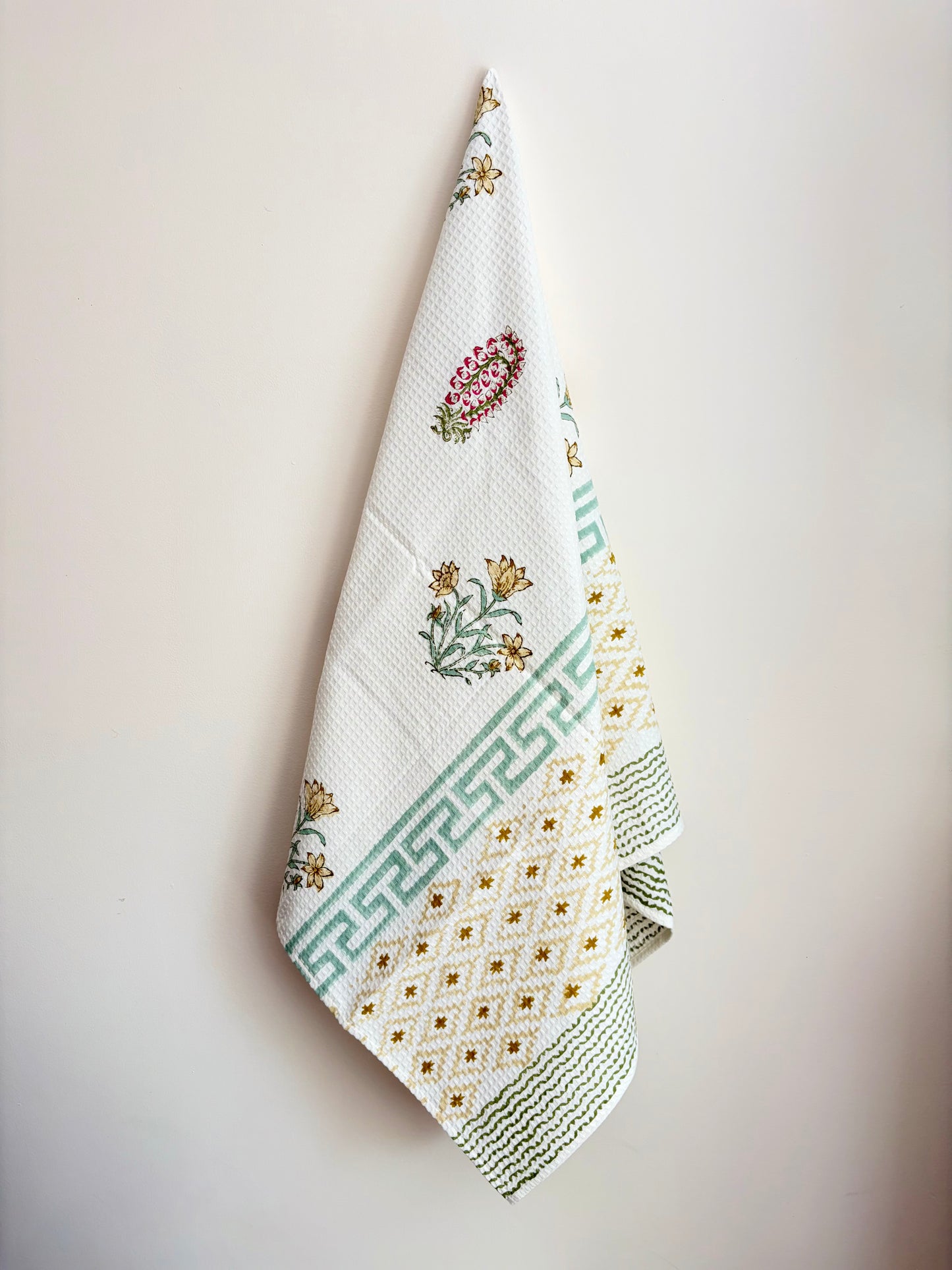 House of Mulmul - Cotton Bath Towel. Floral patterned towel hanging against a plain background with geometric pattern.