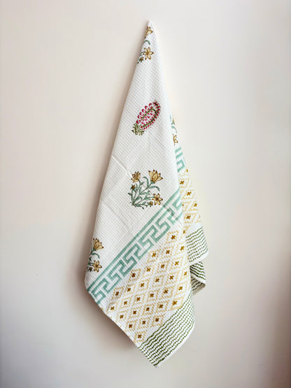 House of Mulmul - Cotton Bath Towel. Floral patterned towel hanging against a plain background with geometric pattern.