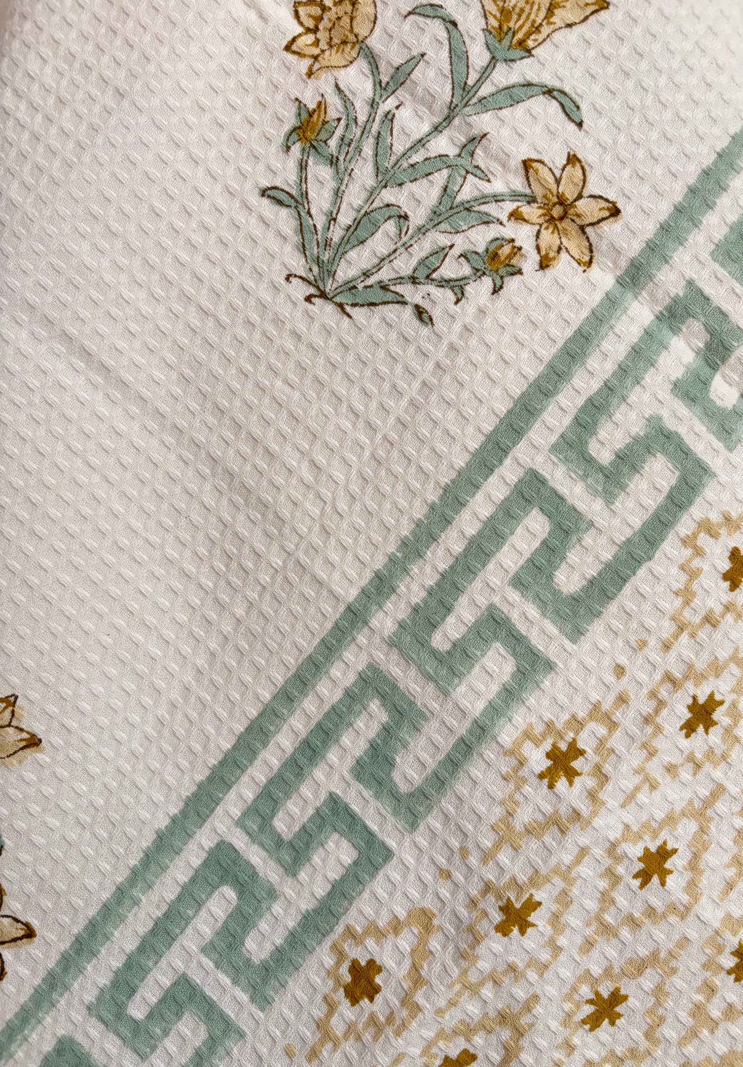 House of Mulmul - Cotton Bath Towel. Floral patterned towel hanging against a plain background with geometric pattern.