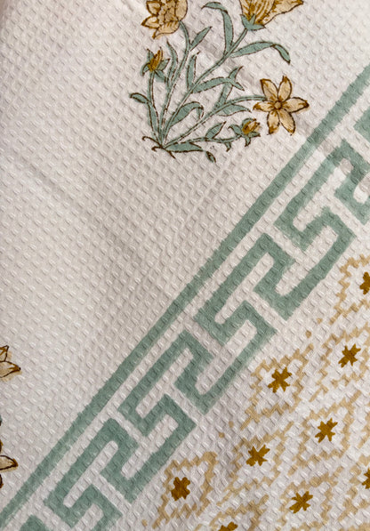 House of Mulmul - Cotton Bath Towel. Floral patterned towel hanging against a plain background with geometric pattern.