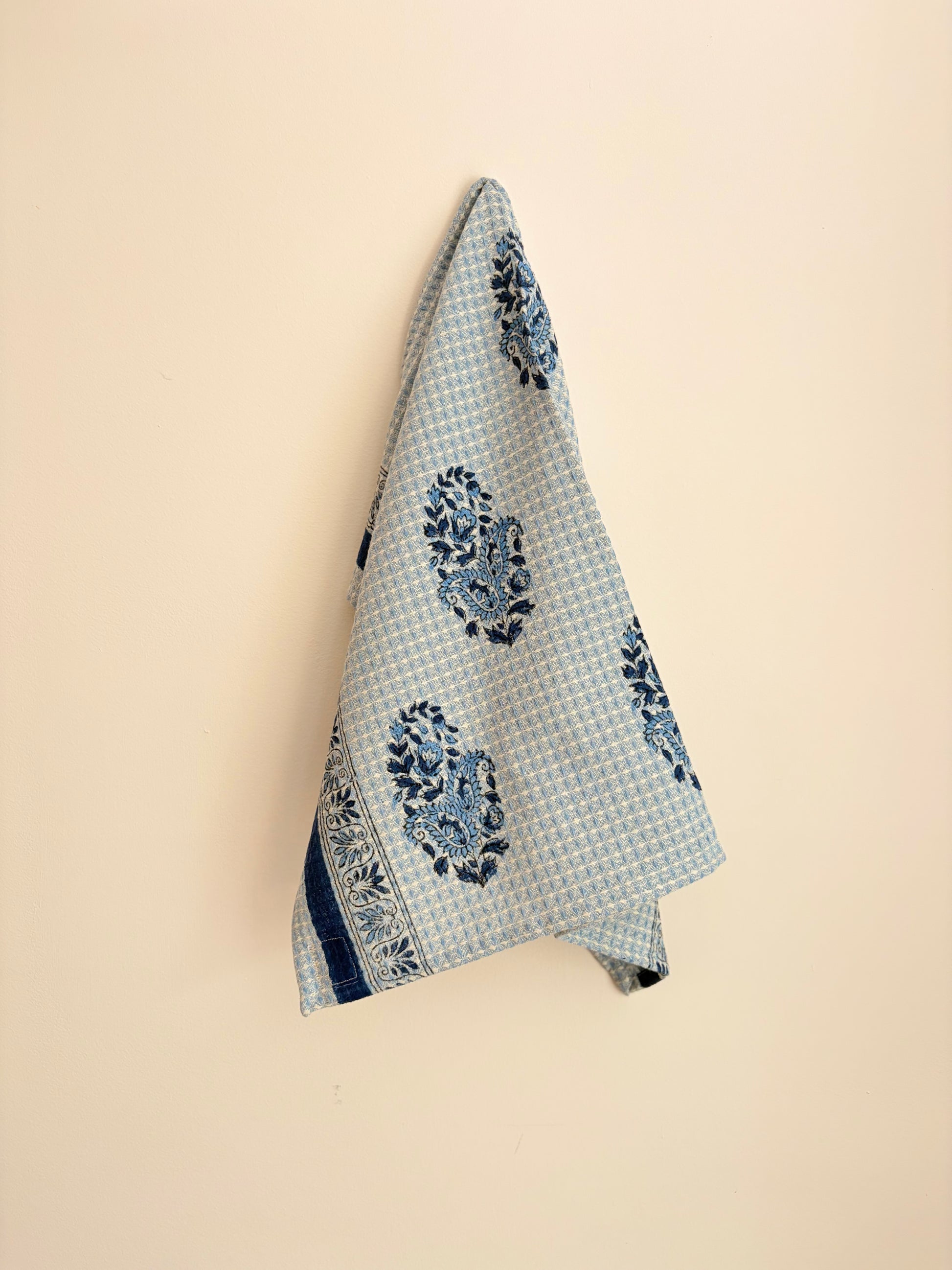 House of Mulmul - Cotton Hand Towel. Blue patterned towel hanging on a beige wall