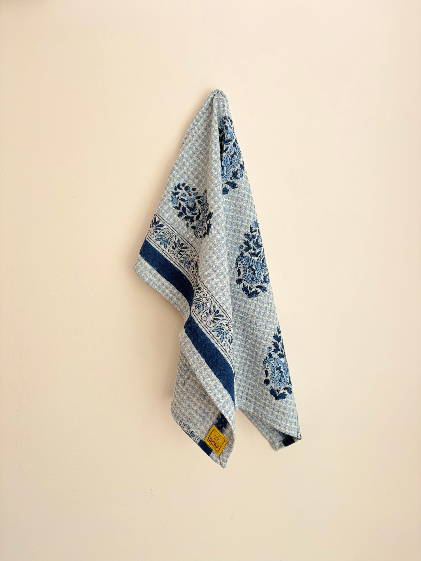 House of Mulmul - Cotton Hand Towel. Blue and white patterned towel hanging on a beige wall