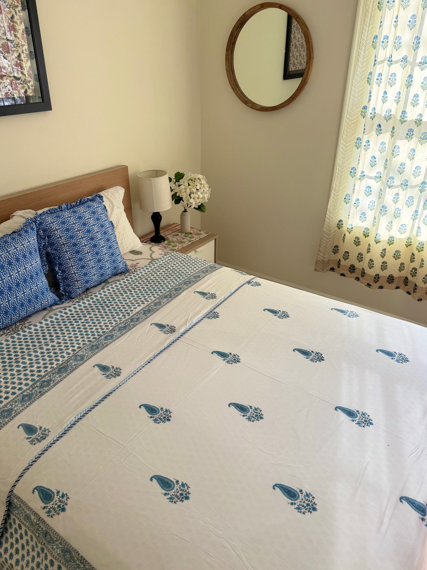 House of Mulmul - Coverlet Dohar blanket. Bedroom with reversible cotton coverlet blanket. Muslin dohar with boota paisley leaf and blue and grey colors, white background. Bedroom with floral curtains, mirror.