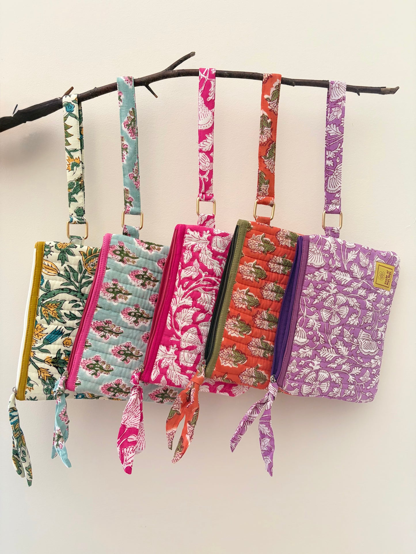 Hand Block Printed Quilted Travel Wristlet Pouch & Organizer. Colorful fabric bags with straps hanging on a branch against a white background
