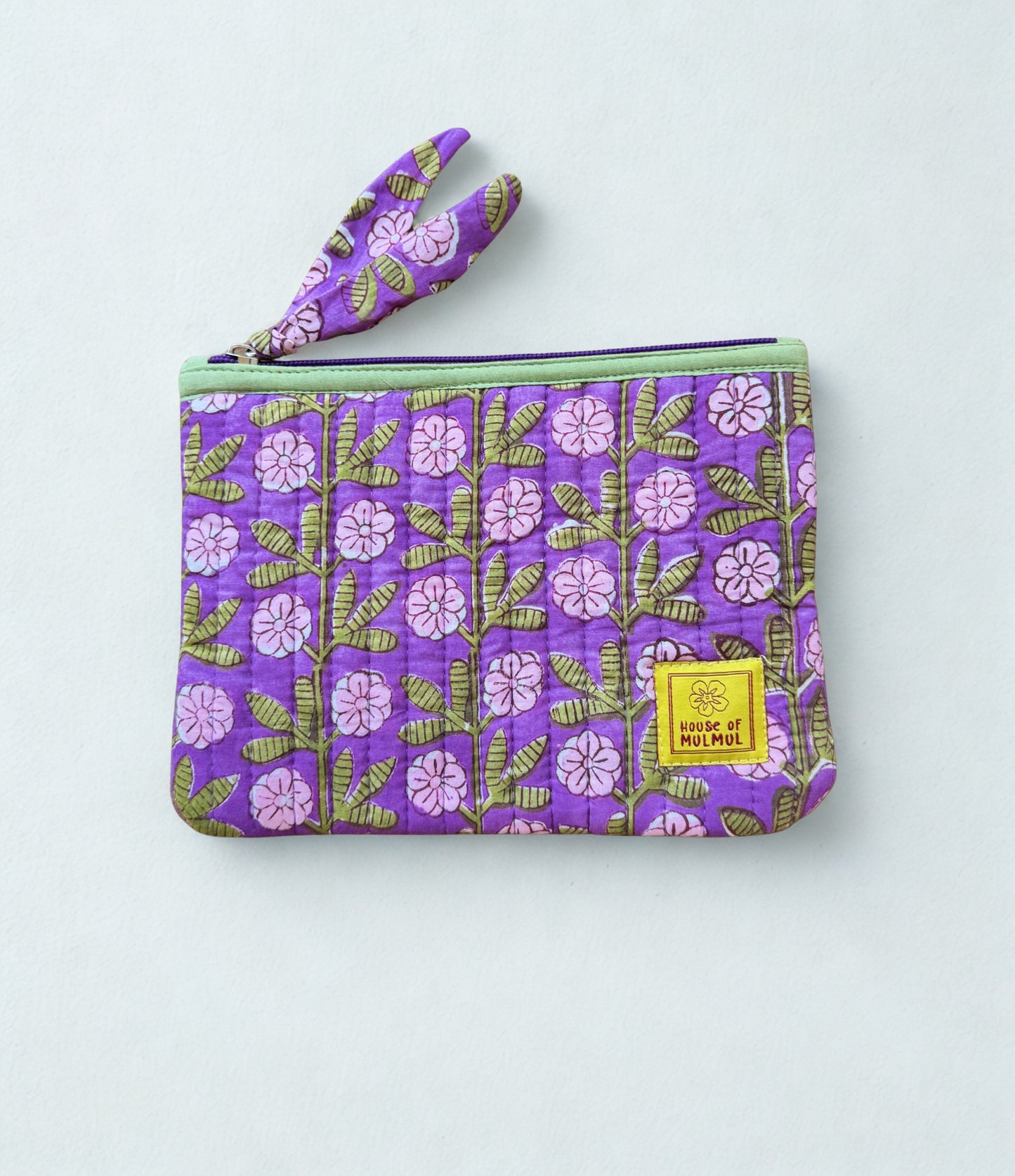 House of Mulmul - Quilted Flat Passport Pouch. Purple floral patterned pouch with a yellow label on a light gray background.