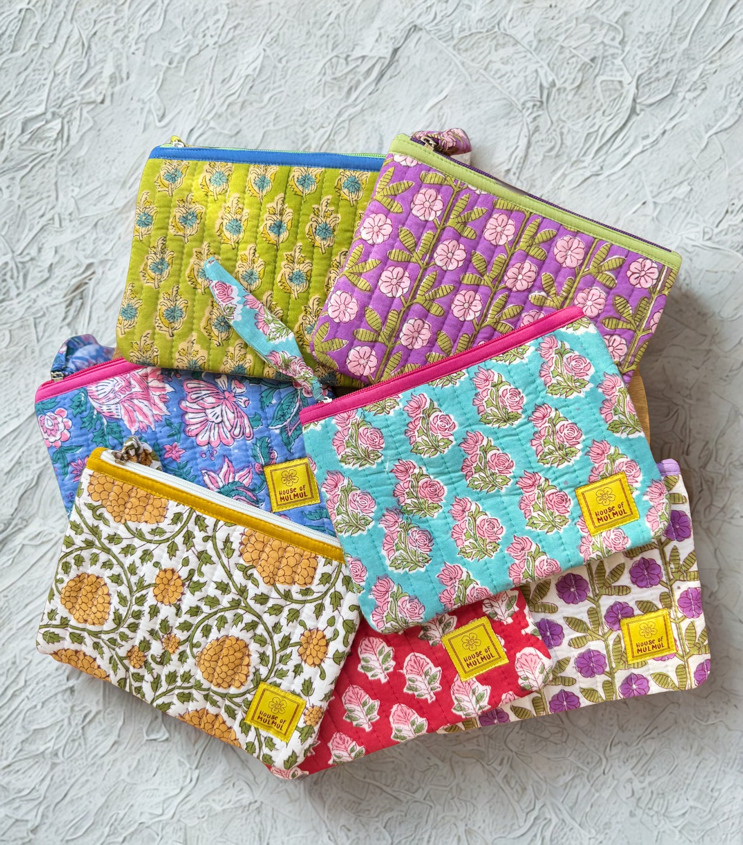 House of Mulmul - Quilted Flat Passport Pouch. Set of colorful patterned pouches on a textured surface.