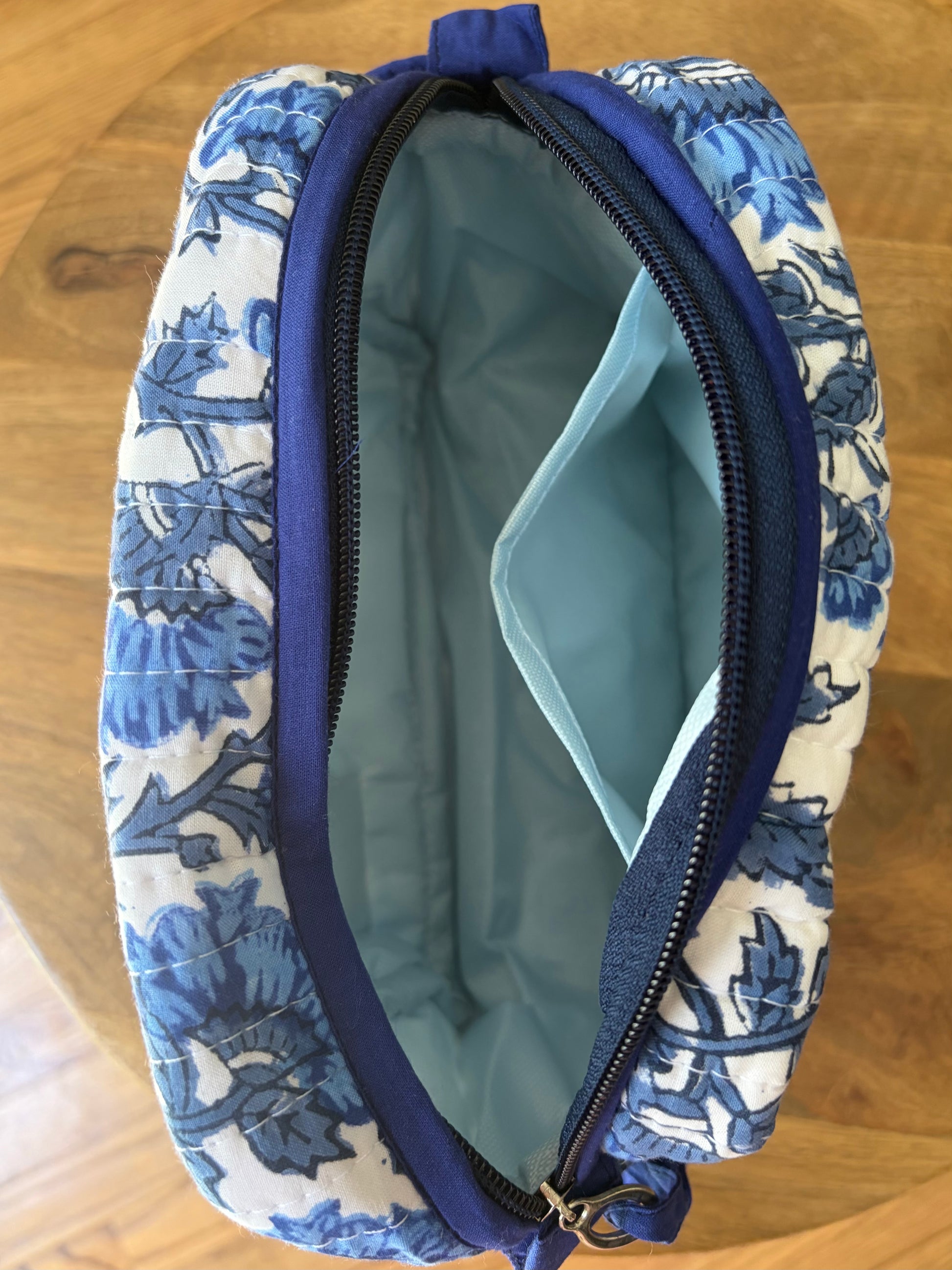 House of Mulmul - Quilted Blockprint Travel Makeup pouch set. Blue and white patterned pouch with a zipper on a wooden surface