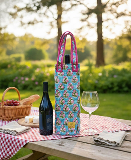 House of Mulmul - Quilted Wine Tote Bag. Floral wine bottle bag on a picnic table with a bottle of wine, glass, and basket in a garden setting.