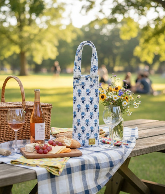 House of Mulmul - Quilted Wine Tote Bag. Picnic setup with a floral-patterned bottle bag, wine, grapes, and bread on a checkered tablecloth in a park.