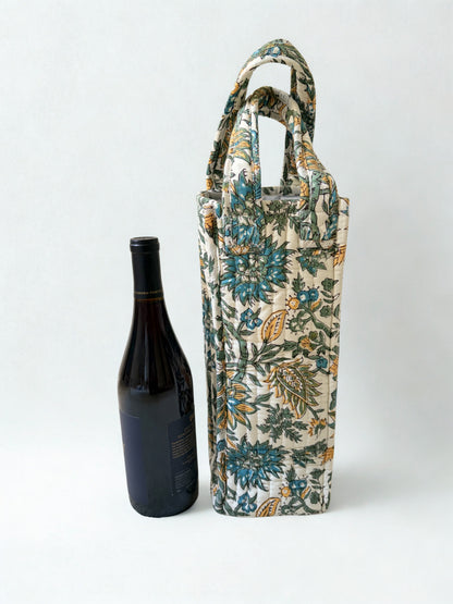 House of Mulmul - Quilted Wine Tote Bag. A tall fabric wine bottle carrier with a floral print in blue, green, and beige, shown next to a dark wine bottle on a light gray background.