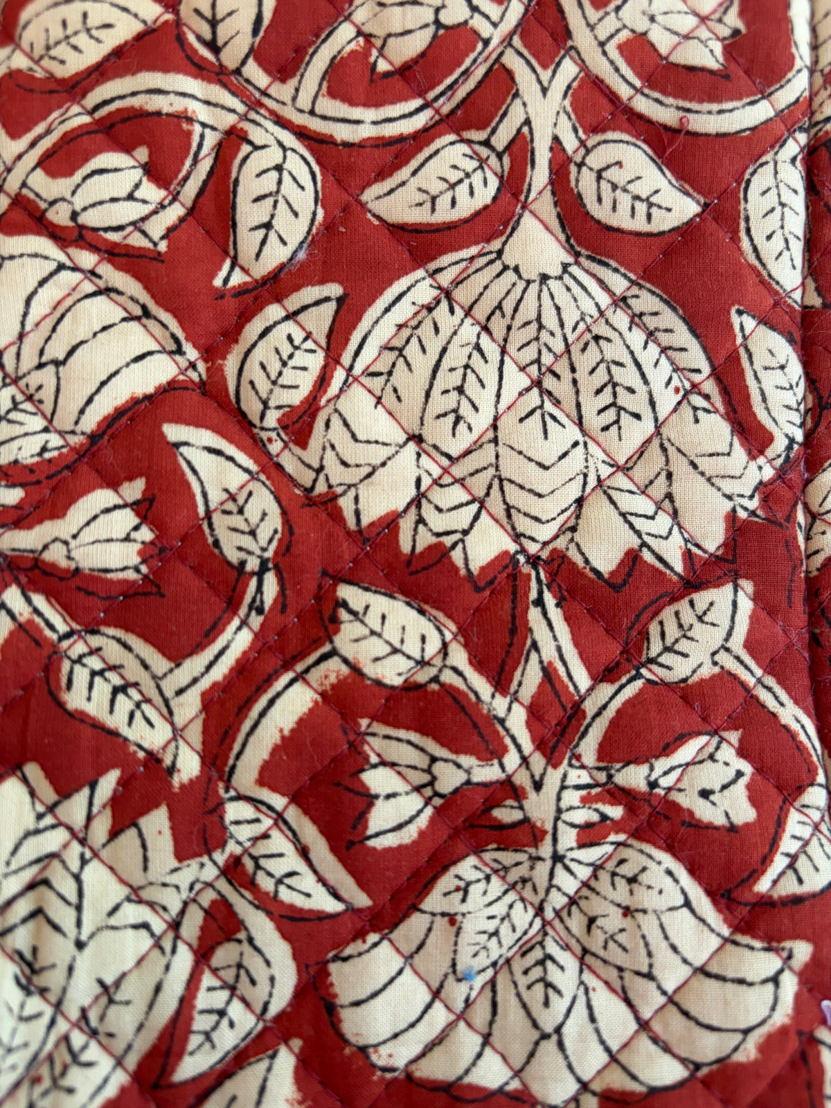 House of Mulmul - Quilted Wine Tote Bags. A close-up of a quilted textile featuring a red and cream floral block-print pattern with black hand-stitched leaf details.