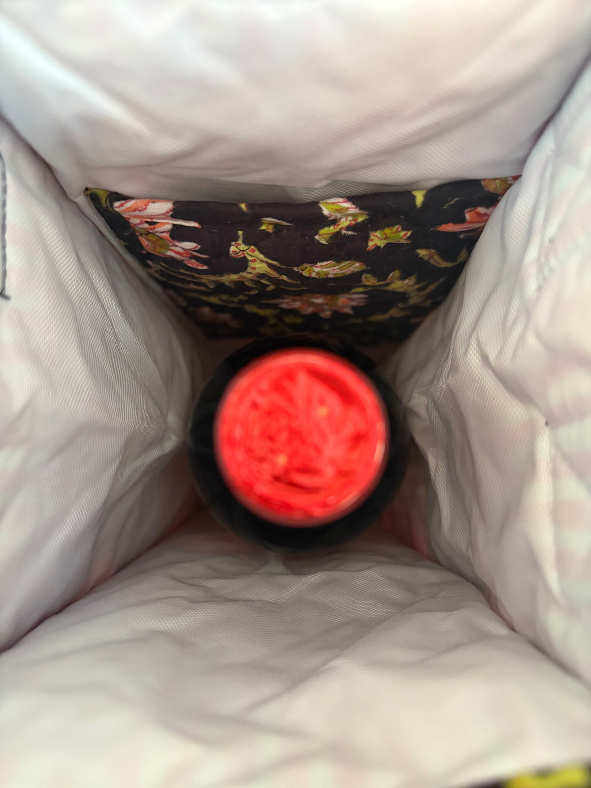 House of Mulmul - Quilted Wine Tote Bags. A close-up view from inside a white insulated bag, showing a black bottle with a bright red cap or lid insert.