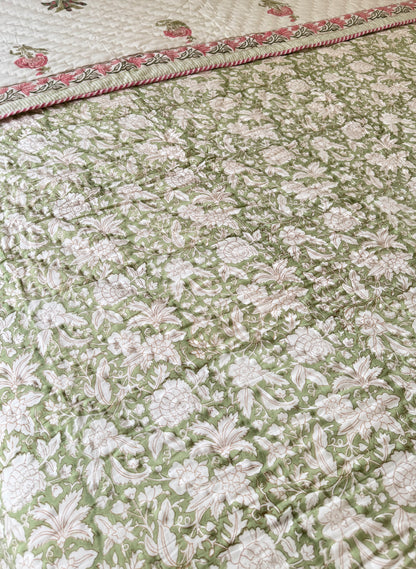 House of Mulmul - Blockprint Cotton Quilt Reversible. A close-up of a quilted cotton quilt featuring an all-over floral pattern in sage green and cream, with a decorative border showing pink and green floral details.