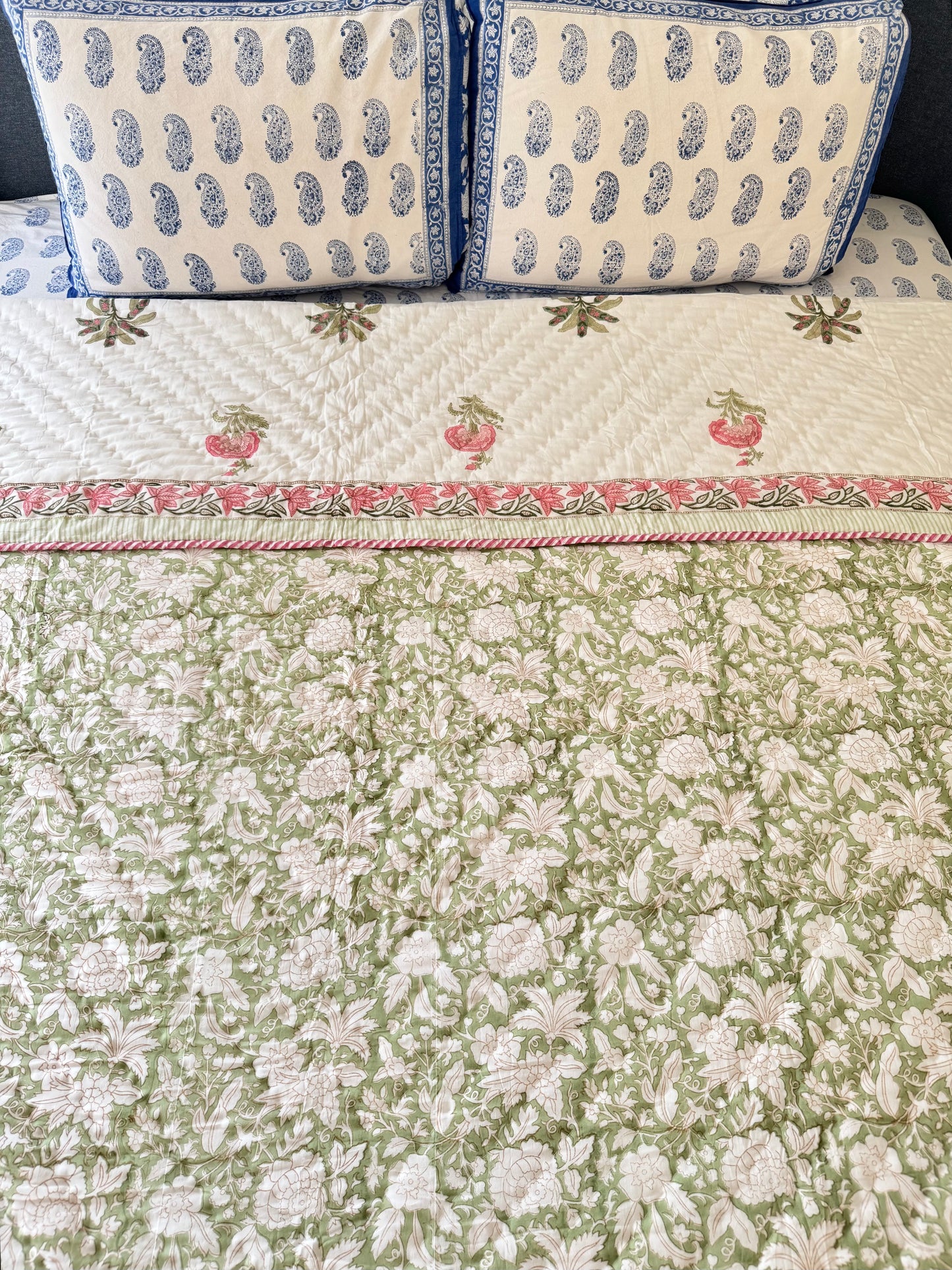 House of Mulmul - Blockprint Cotton Quilt Reversible. A green and white floral quilted bedspread with a pink and white border, styled on a bed with two matching blue and white patterned pillows.