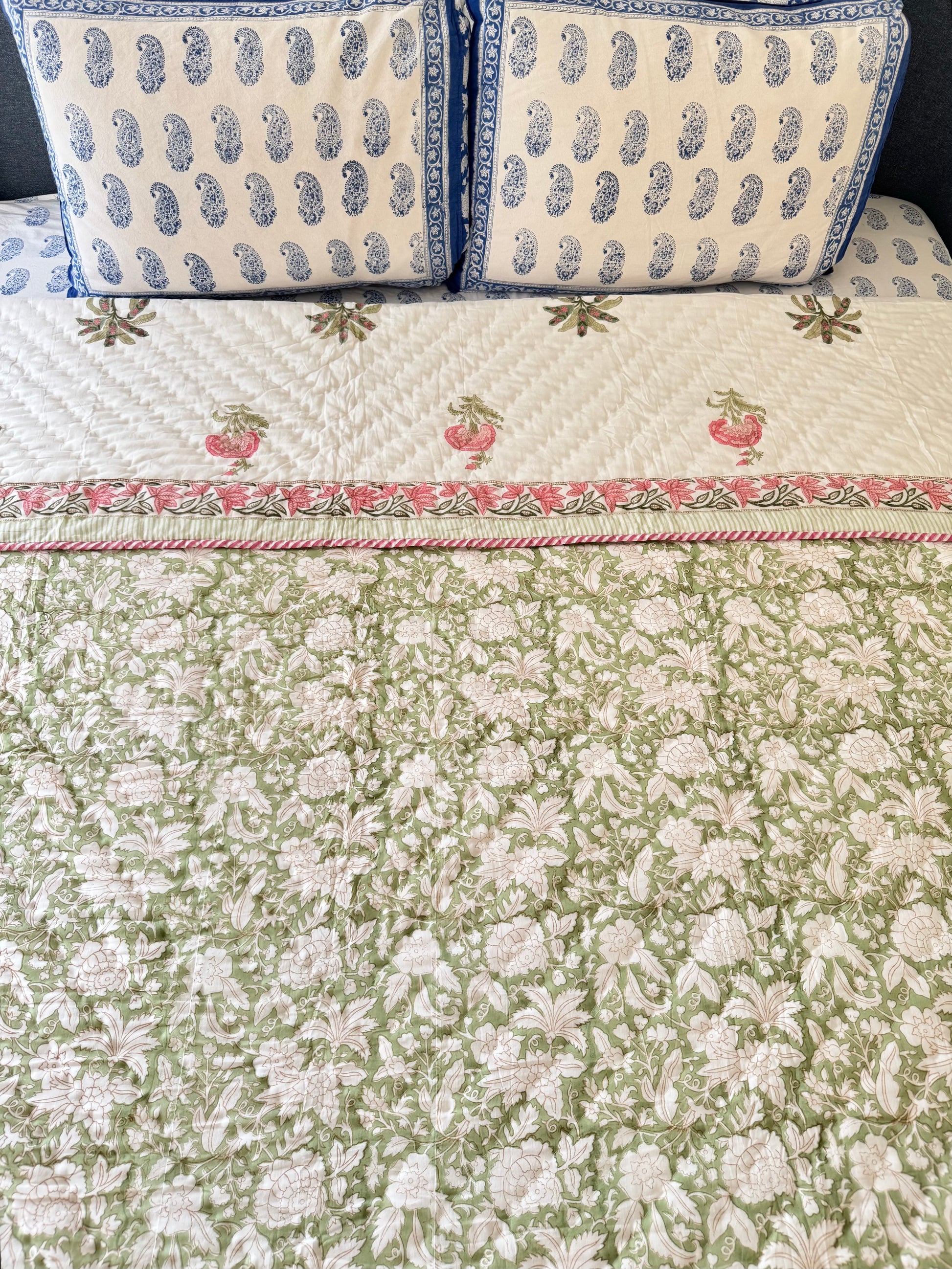 House of Mulmul - Blockprint Cotton Quilt Reversible. A green and white floral quilted bedspread with a pink and white border, styled on a bed with two matching blue and white patterned pillows.