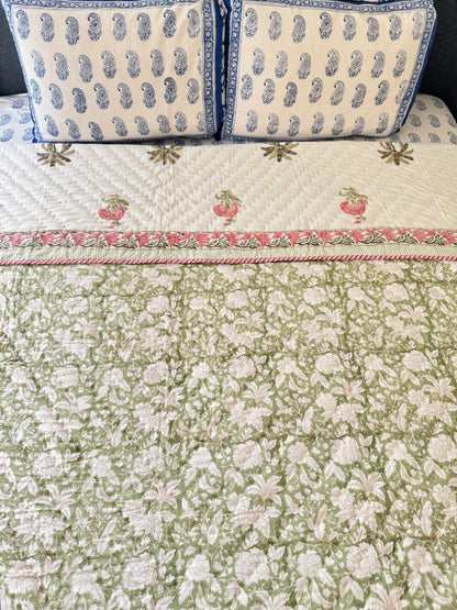House of Mulmul - Blockprint Cotton Quilt Reversible. A green and white floral quilted bedspread with a pink and white border, styled on a bed with two matching blue and white patterned pillows.