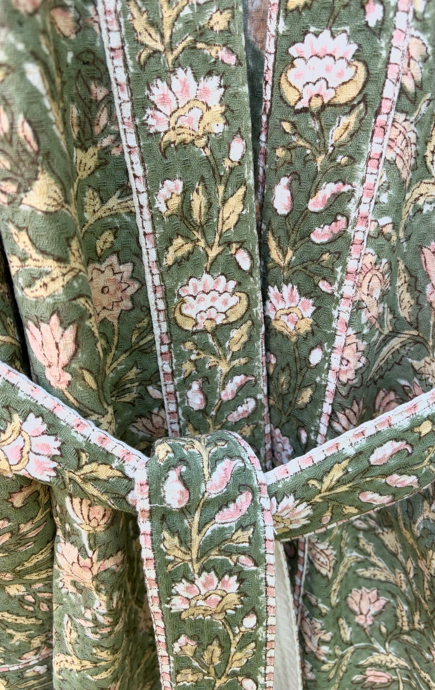 House of Mulmul - Blockprinted Cotton Bathrobe. Close-up of a green floral patterned cotton bathrobe with pink flowers and white stems.