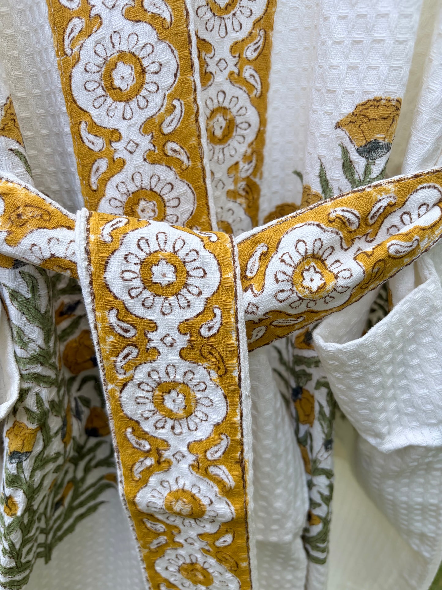 House of Mulmul - Blockprinted Cotton Bathrobe. Close-up of a bathrobe with intricate yellow and white patterns on a white background