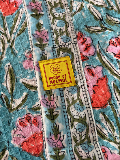 House of Mulmul - Blockprinted Cotton Bathrobe. A close-up of a colorful floral bathrobe with vertical patterned bands and a yellow square patch reading 'HOUSE OF MULMUL'.