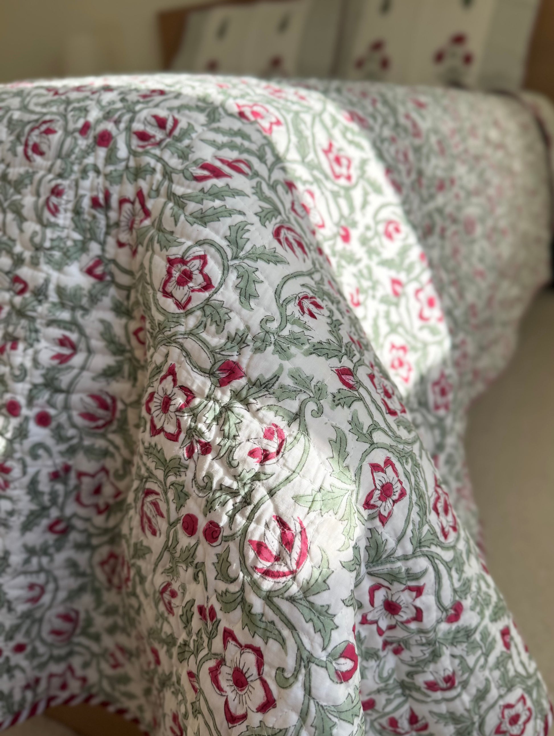 House of Mulmul - Blockprinted Cotton Bedcover Reversible Muslin. Close-up of a floral-patterned cotton bedcover with red and green design on a neutral background