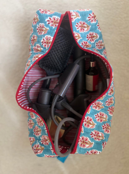 House of Mulmul - Blockprinted Cotton Hair Tool Bag. Floral-patterned  Dyson hair dryer straightener kit hair tool bag containing a hair dryer, bottle, and other items on a beige surface.