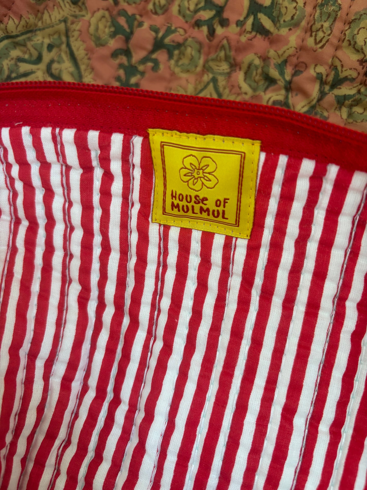 House of Mulmul - Blockprinted Cotton Hair Tool Bag. Red and white striped hair tool bag with a yellow label reading 'House of Mulmul' on a floral background.