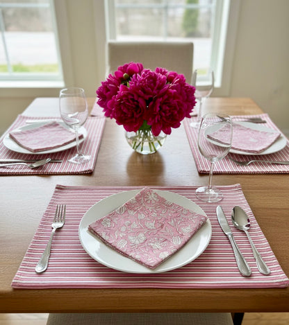 House of Mulmul - Blockprinted Cotton Mats and Napkins. Dining table set with pink placemats, napkins, and a vase of flowers.