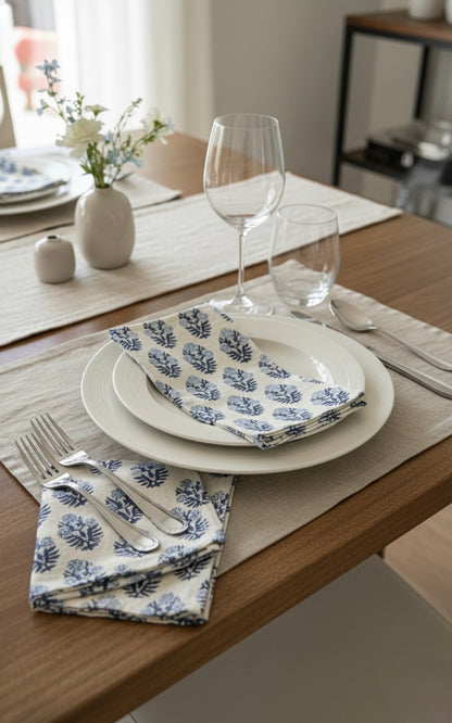 House of Mulmul - Blockprinted Cotton Napkins. Dining table setting with plates, glasses, and floral napkins on a wooden table.