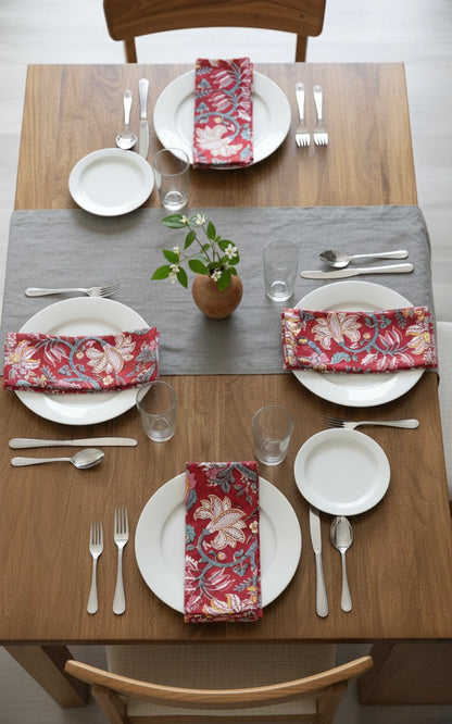 House of Mulmul - Blockprinted Cotton Napkins. Dining table set with plates, silverware, and floral napkins on a wooden table.