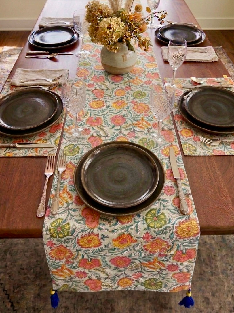 House of Mulmul - Blockprinted Cotton Reversible Table Runner & Mats set. Dining table set with floral table runner, plates, and cutlery on a wooden floor.